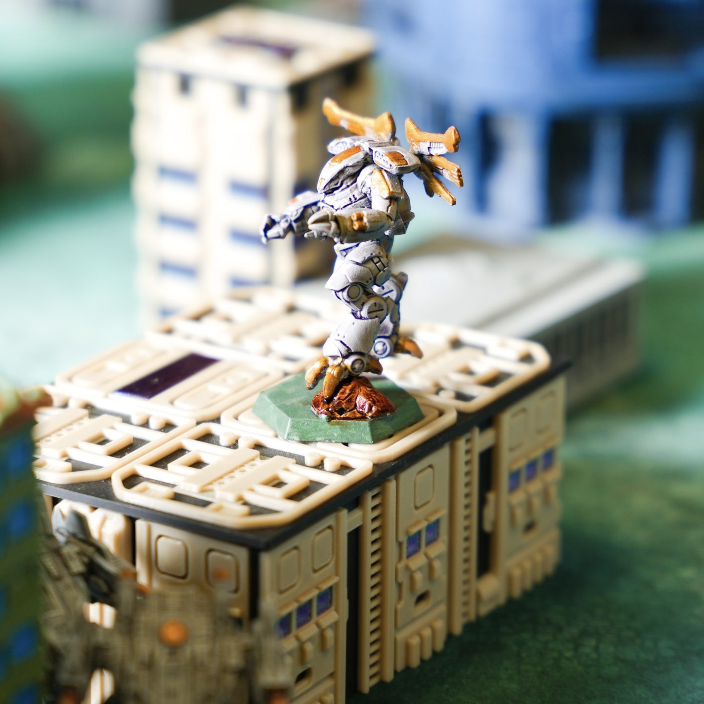 A painted BattleTech mech miniature perched on a terrain building